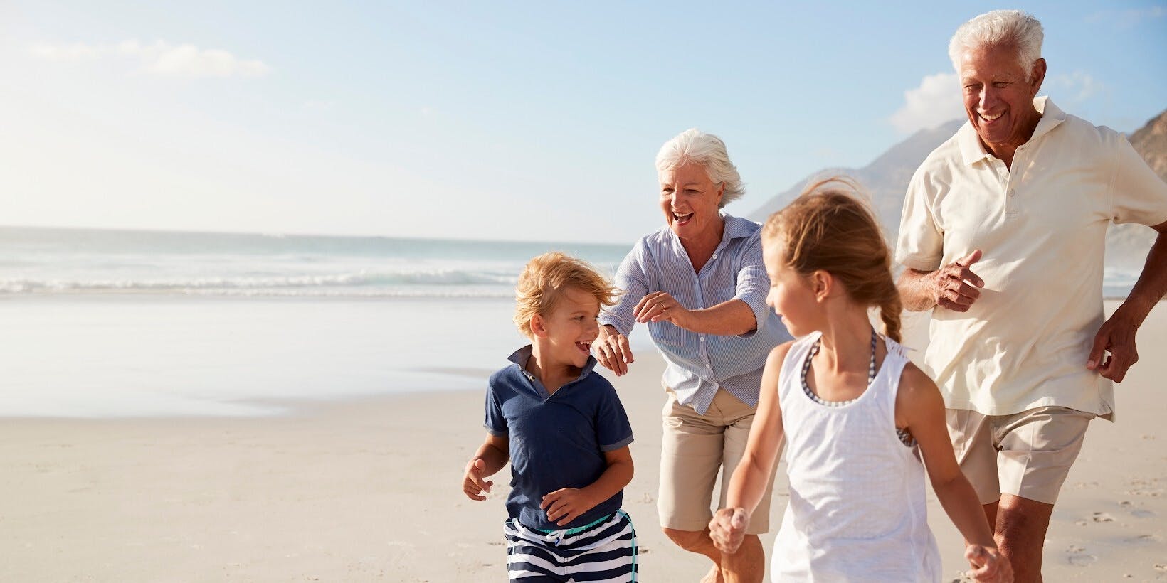 An elderly couple jog after their grandchildren on a sandy beach.